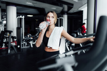 Effective workout, sports girl drinks water after cardio in the gym