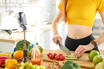 cropped food blogger redhead woman in yellow top cutting cucumber, showing at camera