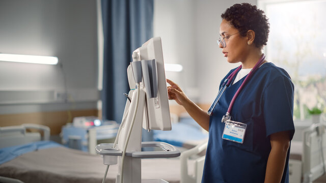 Hospital Ward: Beautiful Black Female Head Nurse, Doctor, Surgeon Uses Health Care Vitals Monitoring Computer Machine. Modern High Tech Clinic With Advanced Equipment And Professional Staff