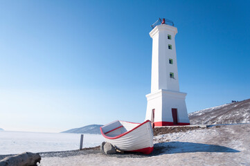 Beautiful white lighthouse and wooden boat on the coast of the Nagaev Bay in Magadan in Russia, on...