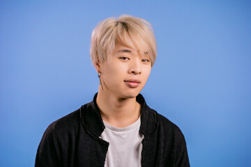 Portrait of stylish korean man looking to camera. Asian guy with dyed blonde hairstyle in studio on bright blue background.