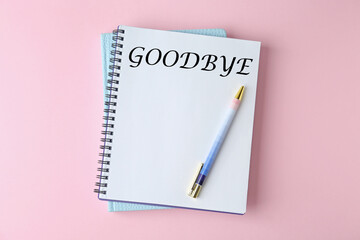 Notebook with word Goodbye on pink background, top view