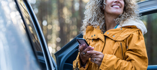Happy adult woman use phone outside the car during outdoor travel transport vacation - concept of...