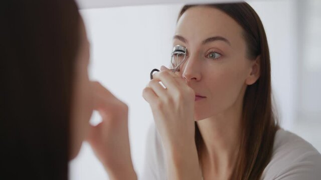 Female curling eyelashes near mirror