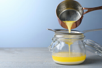 Pouring clarified butter into jar on grey table. Space for text