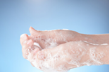 Woman hands in soapsuds, on blue background close-up.