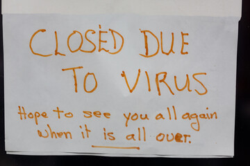 A handwritten sign in a shop window announcing that the shop will be closed due to the virus and hope to see customers again once the pandemic is over
