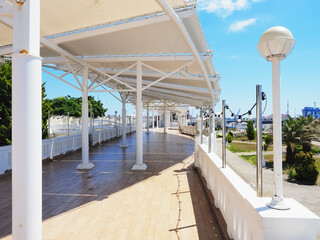 Walking area with a white fence along and a white canopy on props on a clear summer day under a blue sky