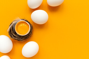 White eggs and egg yolk into nest on yellow background. Top view. Flat lay. Easter celebration
