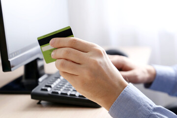 Fototapeta premium Man holding credit bank card types on PC keyboard. Concept of online shopping and payment, financial transaction