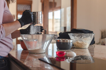 Mujer joven con guantes en su cocina mientras tamiza la harina en un recipiente de cristal. Concepto de cocinar pizza casera. Hacer pan en casa.