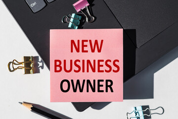 NEW BUSINESS OWNER note is written on a paper sticker on a laptop keyboard.