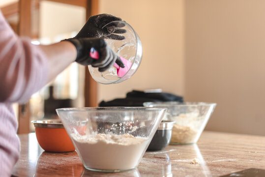 Una mujer vertiendo ingredientes con una espátula de silicona en un recipiente de vidrio con harina en la encimera de la cocina de su casa. Concepto de cocina casera. Hacer pizza y pan en casa.