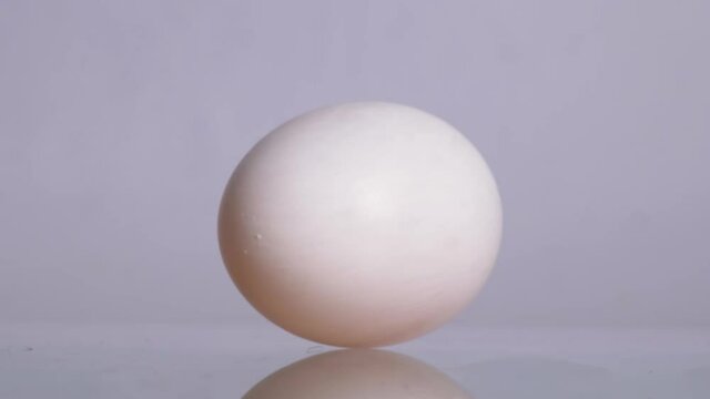 Happy Easter. White chicken egg spinning and rolling on a white background with beautiful reflection