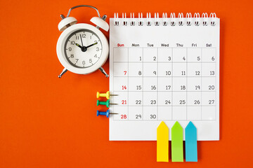 opened calendar with paper tag , alarm clock and thumbtacks on grunge orange paper background
