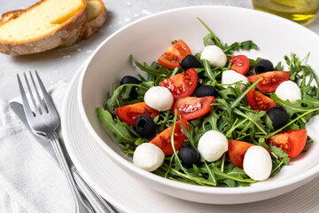 Lunch in Italian restaurant. mediterranean diet  food  salad with arugula mozzarella tomatoes and olives, olive oil and fresh bread 