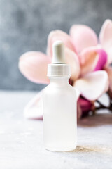 Serum with floral magnolia extracts for skincare. Nature cosmetics in glass bottle with a pipette and with flowers on grey background. Organic Spa Cosmetic With floral Ingredients. 