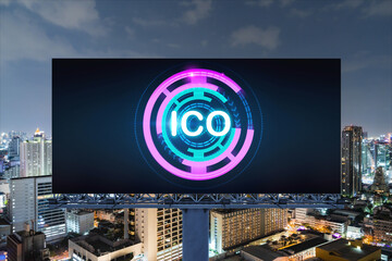ICO hologram icon on billboard over panorama city view of Bangkok at night time. The hub of blockchain projects in Southeast Asia. The concept of initial coin offering, decentralized finance