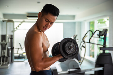 Fototapeta na wymiar Muscular bodybuilder guy lifting weights in gym.