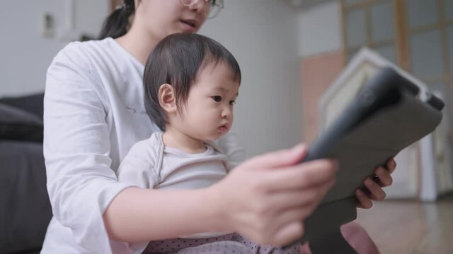 Caring single parent, young mother babysitter with little preschool kid or daughter on her lap, learning reading a fairy tale story on tablet, concept bonding enjoying family lifestyle hobby at home