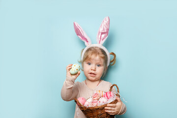 Portrait of a cute little girl dressed in Easter bunny ears holding colorful eggs on blue background