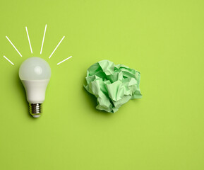 crumpled colored balls of paper and glass white lamp on green background