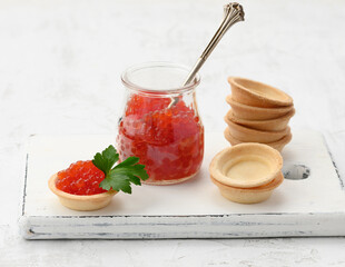 red chinook caviar in a glass jar and round tartlets on a white table