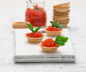 red chinook caviar in a glass jar and round tartlets on a white table