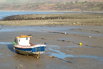 Fototapeta na wymiar Trefor beach, Wales. Secluded sandy beach in a bay on the Llyn Peninsula. Bright sunny spring day. Peaceful countryside. Lone fishing boat on the sands. Landscape aspect. Blue sky - copy space.