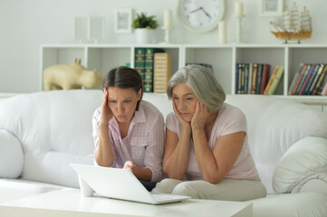 sad mother and daughter sitting at table with laptop, at home