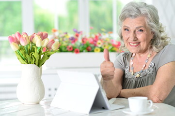 Beautiful senior woman using modern tablet showing thumb up