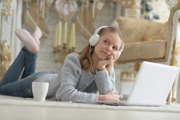 Girl in headphones using laptop while lying on floor