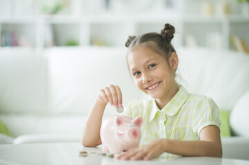Cute little girl with a piggy bank at home