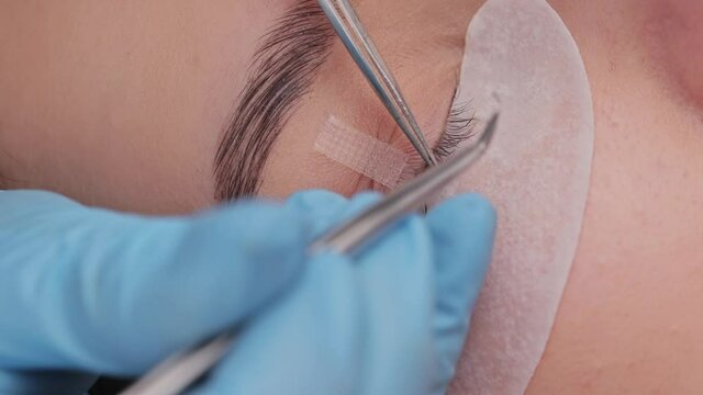 Eyelash extension procedure. The working process of professional beauty master lengthening female lashes. Fake eyelashes. Eyelashes extensions close up. Makeup artist and client in beauty salon