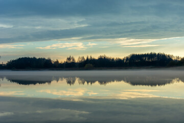 Fog over a calm lake, trees and evening clouds