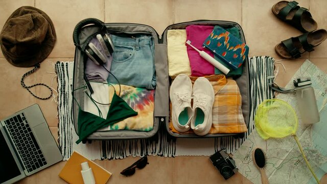 Top view of woman neatly packing and organising summer themed suitcase. Ready for vacation or holidays. Travel blogger essentials, Road trip wanderlust lifestyle. Suitcase packed and ready to go