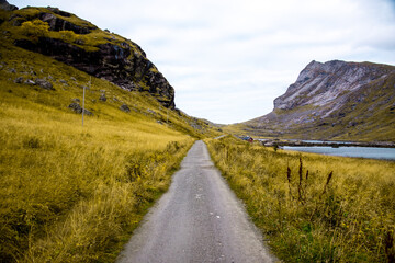 Stone gravel hiking trail leads through rocky and rugged mountain landscape near the famous tourist hotspot Bunes Beach - grass and fjord landscape on Bunes Beach Trail Head, Lofoten Islands, Norway