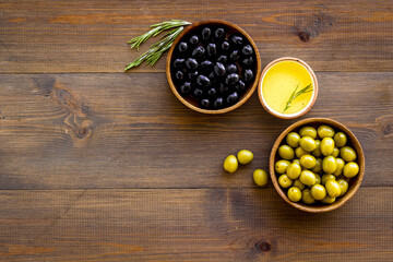 Olives in wooden bowl with oil and rosemary leaves, top view