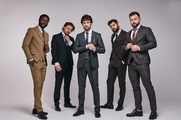 sexy handsome fashion businessmen models dressed in elegant classic suit posing on gray wall indoors