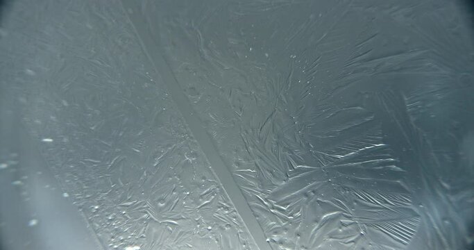 Abstract extreme close up macroscopic shot of water crystallizing and freezing on a glass surface.