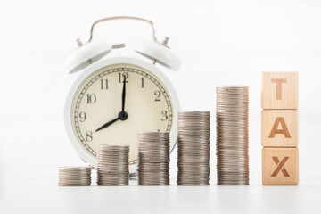 Concept of tax season with wooden blocks, coins and alarm clock.