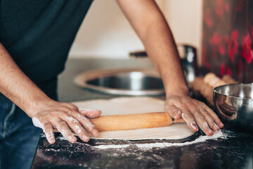 Man makes pizza at home in the kitchen. Rolls out the dough with rolling pin