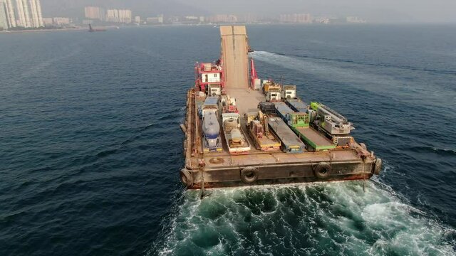 Barge loaded with Concrete mixer trucks pulled to port by a Tugboat in Hong Kong bay, Aerial view.
