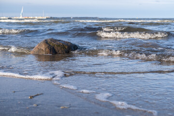 Fototapeta na wymiar Beautiful landscape. Seashore with waves and a large stone, port on the horizon, against the blue sky.