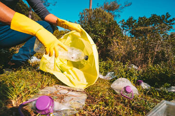 Volunteer in yellow gloves collecting garbage in trash bag outdoors. Picking up garbage in nature. Concept of environmental protection. People and ecology. Save nature.