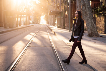 stylish young woman crossing the street at sunset