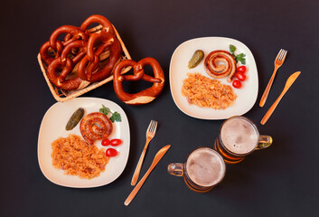 Plates with roasted sausage and stewed cabbage, beer mugs and basket with soft pretzels. Top view.