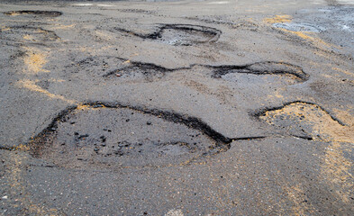 Pits on the road with stones on the asphalt. Destroyed asphalt pavement on the road. Poor road condition requiring repair. View from above. Road construction and repair.
