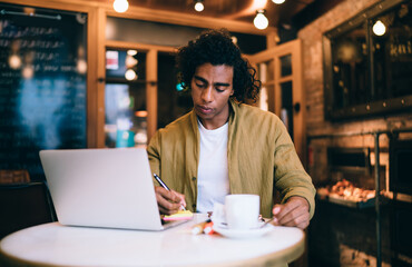 Fototapeta na wymiar Focused ethnic freelancer taking notes in cafe