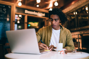 Focused ethnic man writing notes in copybook